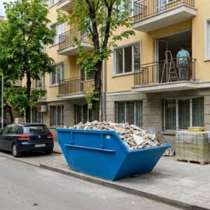 Тествахме пазара: Кои фирми реагират най-бързо при заявка за контейнер за отпадъци? Син метален контейнер, пълен със строителни отпадъци, разположен на тротоар пред жилищна кооперация, доставен чрез услуга за бърза доставка на контейнер за отпадъци София.